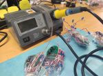 Eine Lötstation mit angeschlossenem Lötkolben, daneben mehrere elektronische Baugruppen mit Drähten und LEDs.