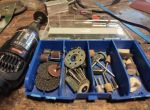 Ein Dremel-Multitool liegt auf einer Werkbank neben einer geöffneten Box mit verschiedenen Schleif-, Fräs- und Polieraufsätzen.